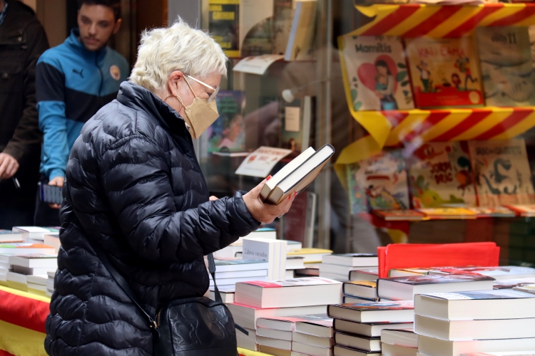 A woman with two books in Lleida in front of a Sant Jordi books stand on April 22, 2022
